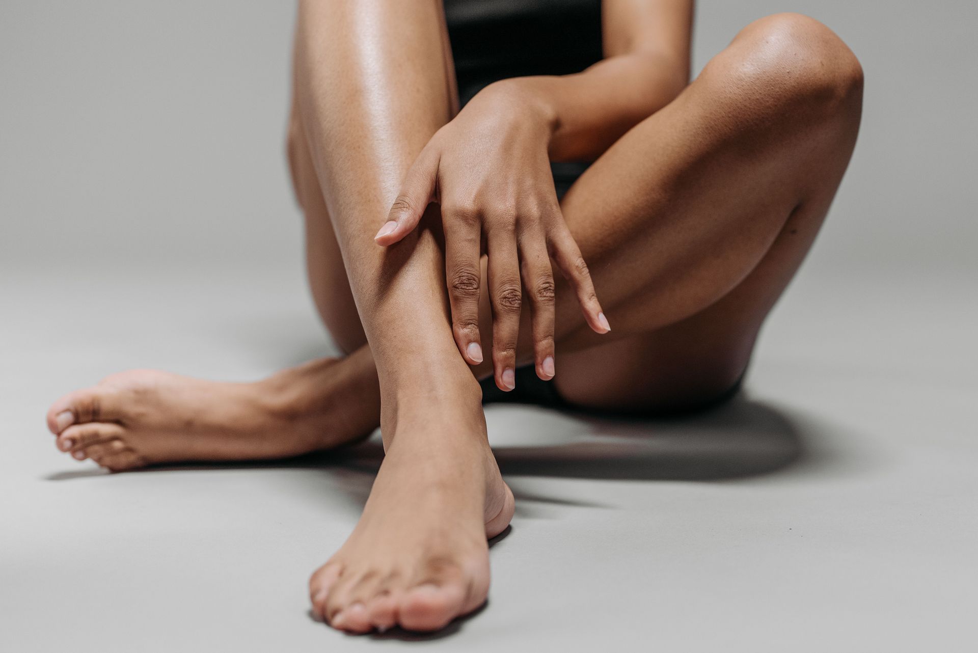 Close-up view of a woman's legs and hands sitting cross-legged on the floor, emphasizing skin tone and texture.